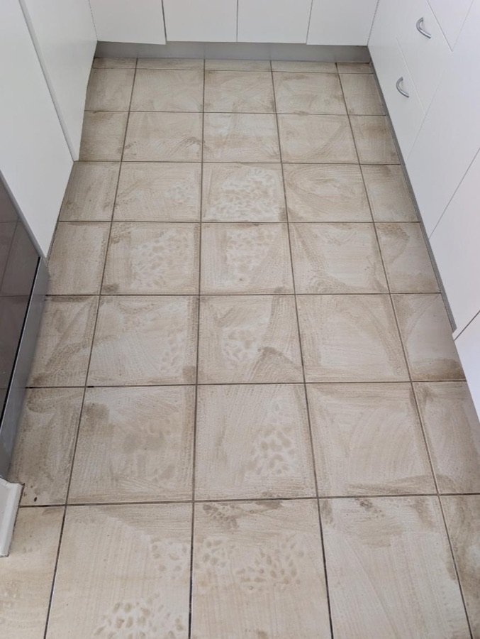 Before: dull kitchen floor tiles with dirty grout and cleaning residue beside white cabinetry