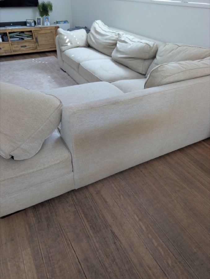 Before: cream fabric corner lounge with visible dirt and staining on the arm and cushions before cleaning